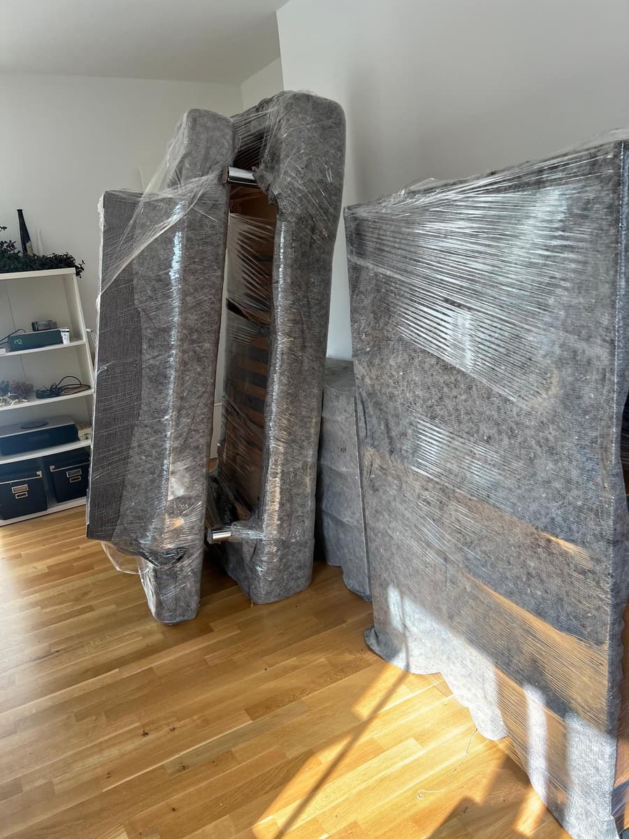 Sofa und Möbelteile, in Umzugsdecken und Stretchfolie eingeschlagen, stehen in einer Wohnung bereit