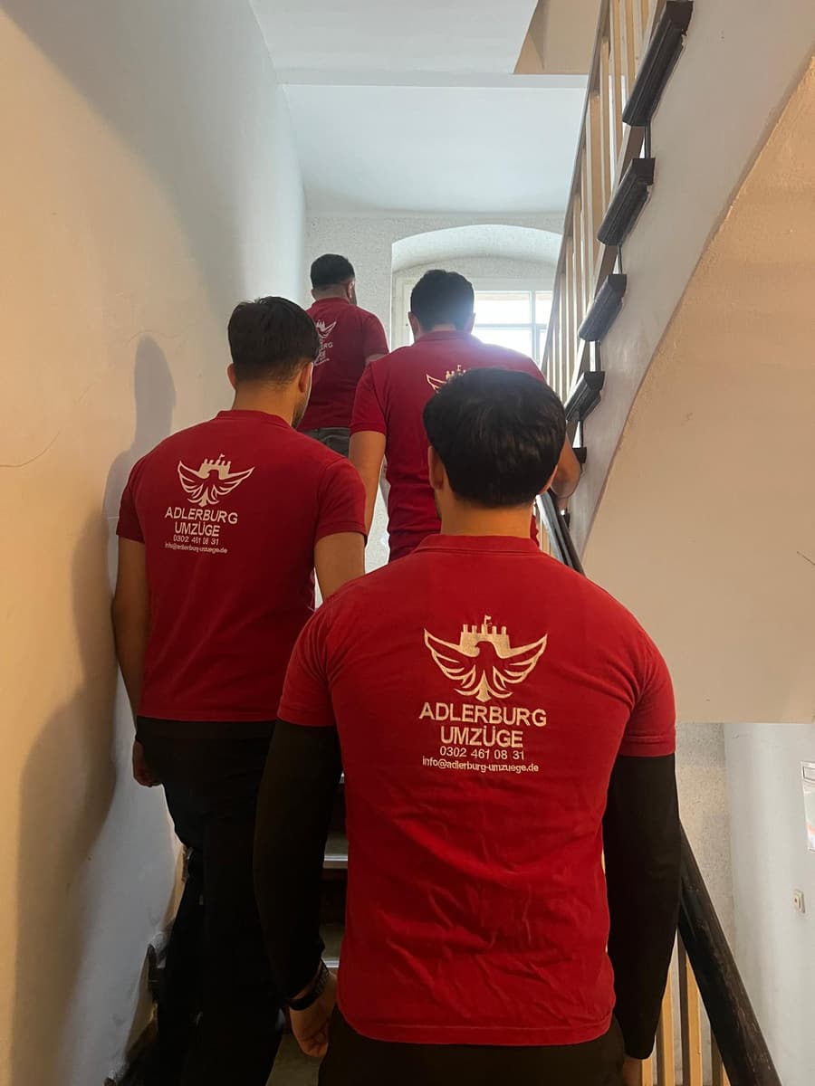 Drei Mitarbeiter in roten Adlerburg-Poloshirts gehen ein Altbau-Treppenhaus hinauf