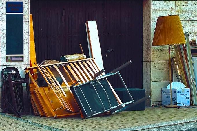 Ausrangierte Holzstühle, Möbelteile und eine Stehlampe vor einem Garagentor, bereit zur Abholung