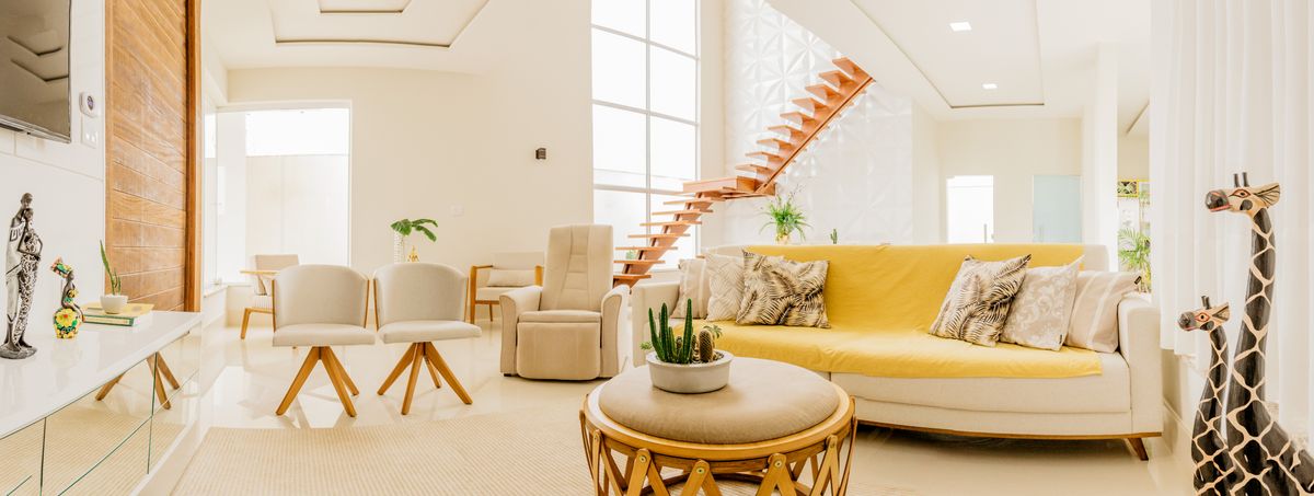 Heller, aufgeräumter Wohnraum mit gelbem Sofa, Sesseln und offener Treppe, freie Böden und viel Tageslicht